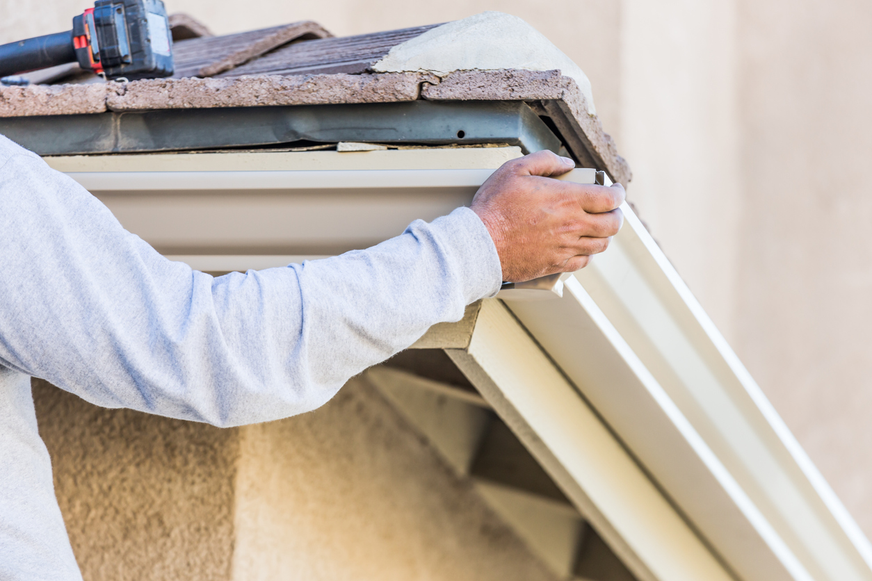 Worker Attaching Aluminum Rain Gutter to Fascia of House Worker Attaching Aluminum Rain Gutter to Fascia of House.